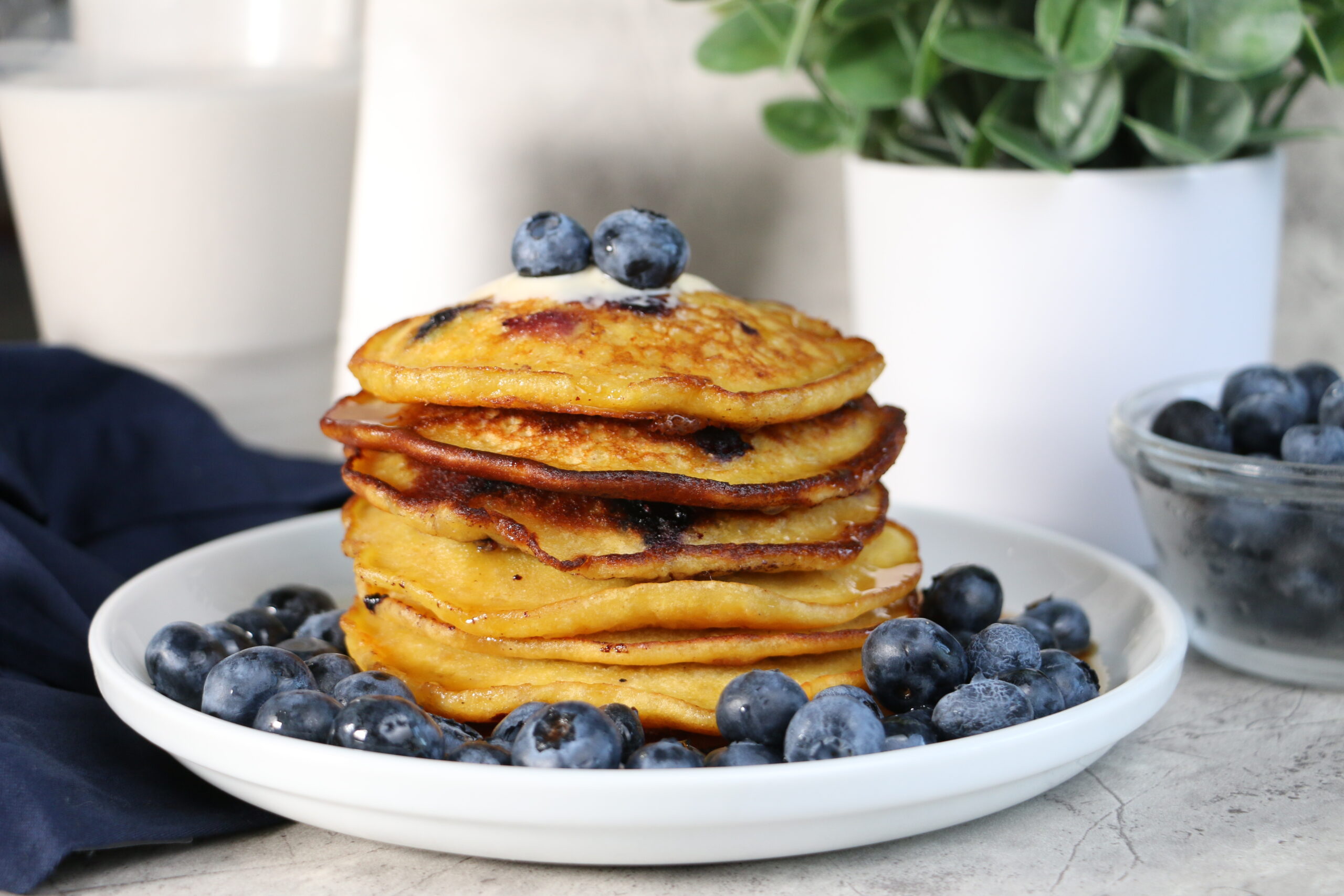 stacked pancakes surrounded by blueberries and a glass of milk